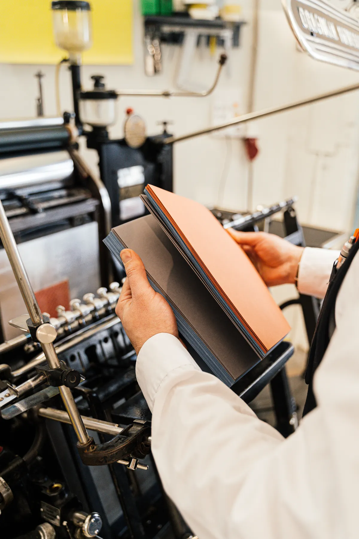 Hände halten frisch bedruckte Papierbögen in einer Druckwerkstatt